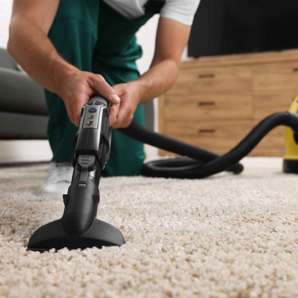 Close-up of a professional using a yellow water extraction vacuum to dry a soaked carpet after indoor flooding.