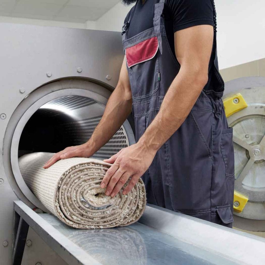 Technician loading a soaked carpet into an industrial drying machine as part of flood water damage restoration and carpet drying process.