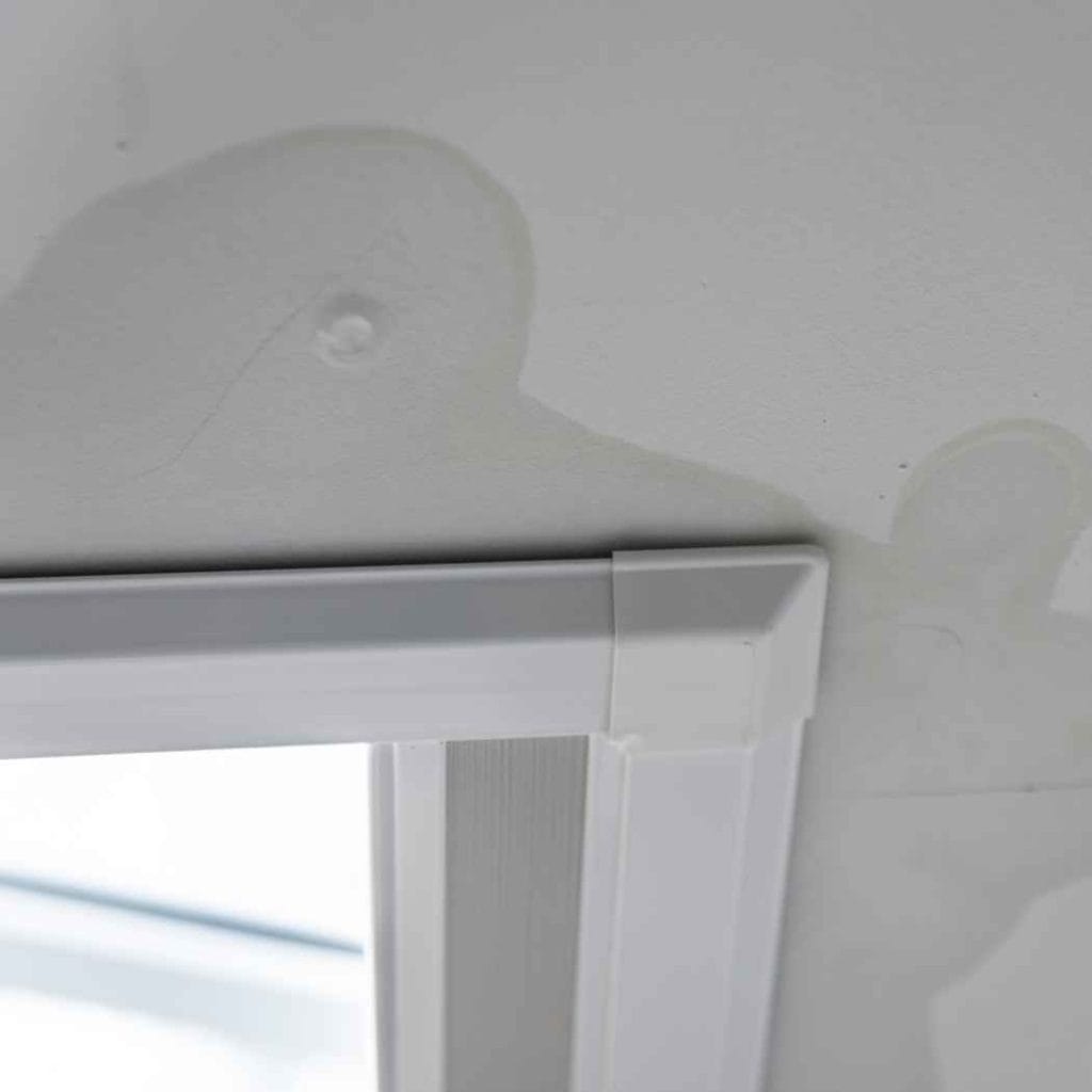 Ceiling water stains and bubbling paint above a window frame, indicating moisture intrusion and potential water damage.
