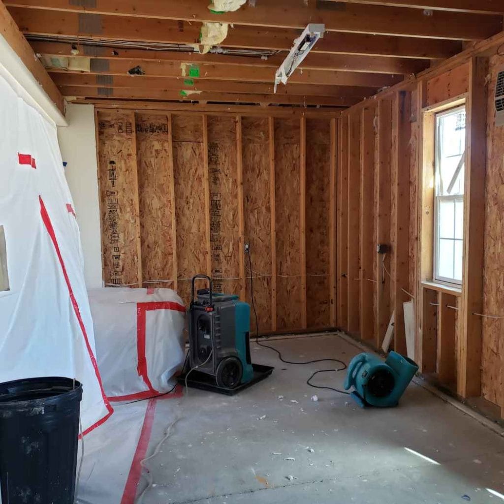 Interior room under flood damage restoration with exposed wall framing, drying equipment, and sealed plastic containment area for moisture and mould control.