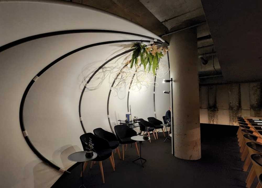 Minimalist and modern interior of Ishizuka restaurant in Melbourne, featuring a sleek curved white wall structure with black circular framing, hanging greenery, and intimate black chairs and tables arranged for fine dining in a sophisticated underground setting.