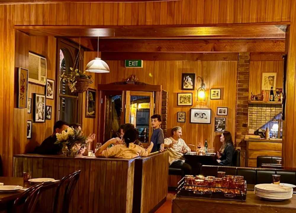 Cosy interior of Leonardo’s Pizza Palace in Melbourne, showcasing wooden-panelled walls, vintage framed photos, and warm ambient lighting. Diners are seated in booths enjoying food and conversation, creating a nostalgic and inviting atmosphere reminiscent of classic Italian-American eateries.